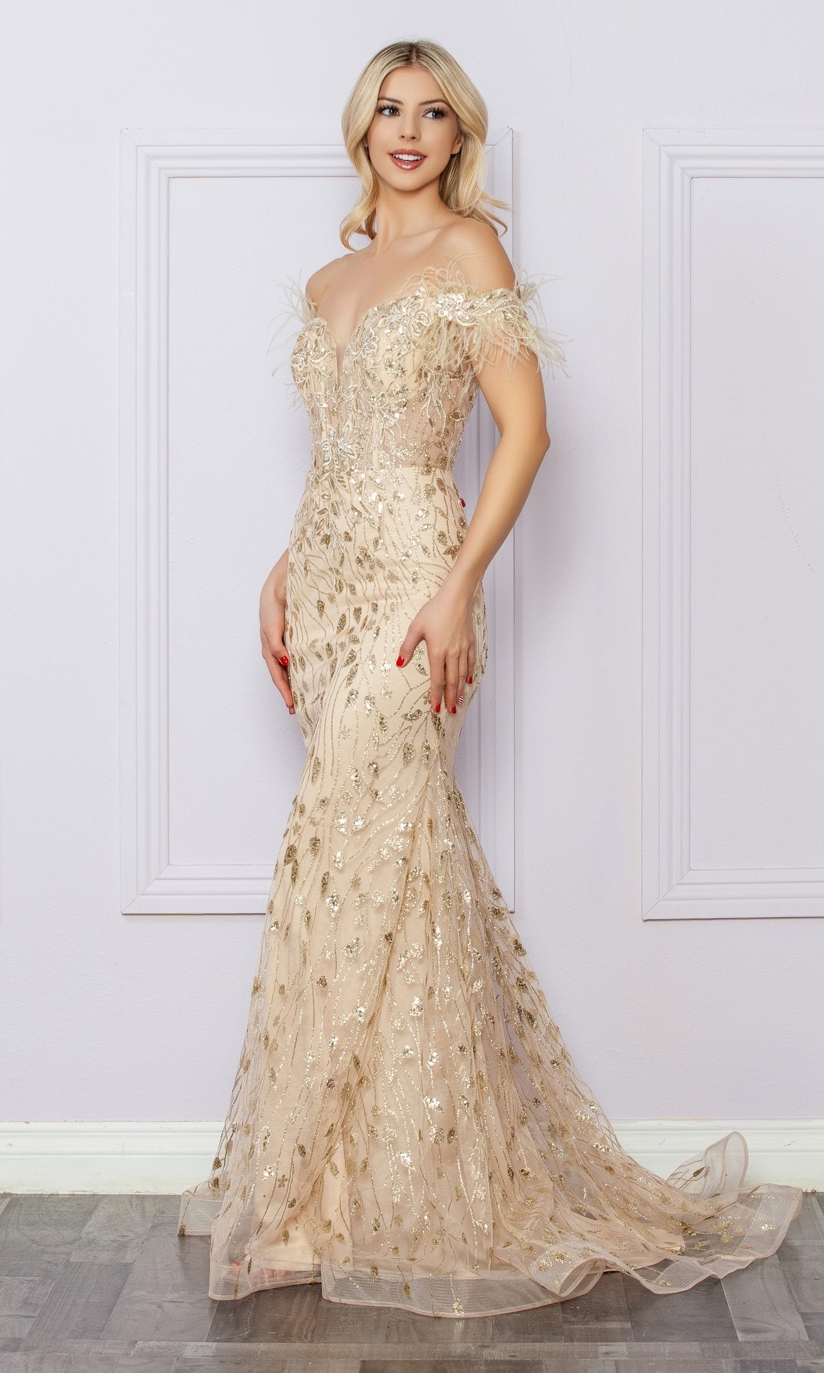 A woman wearing the Sequined Glitter-Print Prom Dress: Nox Anabel L1255, a floor-length gold gown with feather details, stands against a light-colored wall with decorative molding.